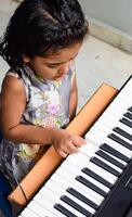Asian cute girl playing the synthesizer or piano. Cute little kid learning how to play piano. Child's hands on the keyboard indoor. photo