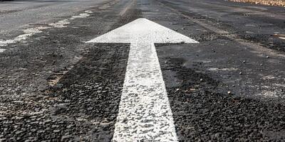 An asphalt road stretches into the distance with a painted white arrow pointing forward, symbolizing motivation, progress photo