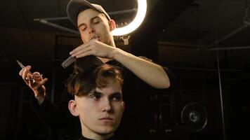 Barber master hairdresser does hairstyle and style with scissors and comb. Concept Barbershop. front view in dark key lightning with warm light photo