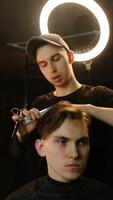 Barber master hairdresser does hairstyle and style with scissors and comb. Concept Barbershop. front view in dark key lightning with warm light photo