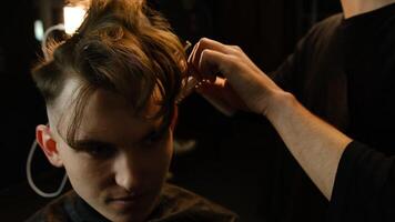 Close up Barber master hairdresser does hairstyle and style with scissors and comb. Concept Barbershop. front view in dark key lightning with warm light photo