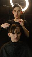 Barber master hairdresser does hairstyle and style with scissors and comb. Concept Barbershop. front view in dark key lightning with warm light photo