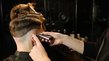 men's hairstyling and haircutting with barber shaving machine, hair cut for male. Hairdresser service with shaver in a modern barbershop in a dark key lightning with warm light back view photo