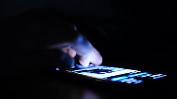 Close up of man finger using and touching on smartphone screen with reflection and black background in the darkness. Social network surfing, instagram or facebook or tiktok photo