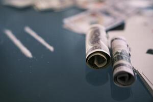 Blured Rolled 100 us dollars, 2 lines of cocaine, illegal drugs on a black glass table. Drug addiction. With selective focus photo