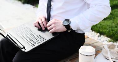 Caucasian bearded business man freelancer working on break with laptop outdoors in park. Male office worker sitting on a bench on a city street park on a modern urban background Workplace outside photo