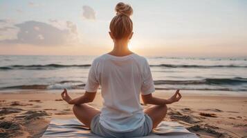 A woman in white tshirt mockup is meditating on the beach at sunset photo