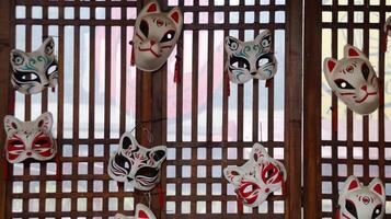 Traditional Japanese Kitsune Masks Displayed on Wooden Lattice Background with Red and White Patterns, Showcasing Cultural and Artistic Heritage in a Rustic Setting photo