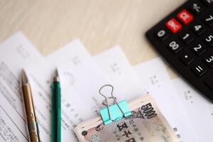 Japanese tax forms lies on table with calculator, pen and japanese yen money bills roll photo