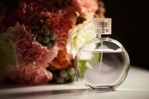 A round bottle of perfume on a dark background, near a bouquet with pink flowers.Aromatherapy and perfumes. photo