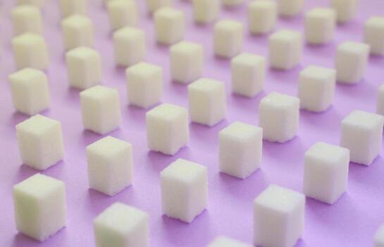 Many small sugar cubes are lined up on a violet background. photo