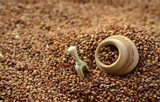 Background image of a large pile of buckwheat, in the middle of which lies a small jug and a wooden spatula for cereals photo
