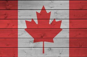 Canada flag depicted in bright paint colors on old wooden wall. Textured banner on rough background photo