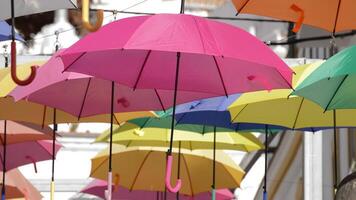 Pink umbrella hanging in a village square with color umbrella heap video