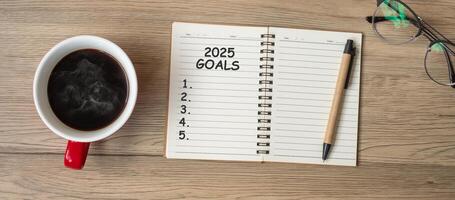 2025 GOAL with notebook, black coffee cup and pen on wood table, Top view and copy space. Happy New Year, Resolution, To do list, Strategy and Plan concept photo