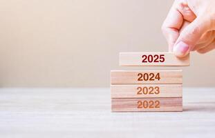 2025 block over 2024 and 2023 wooden building on table background. Business planning, Risk Management, Resolution, strategy, solution, goal, New Year New You and happy holiday concepts photo