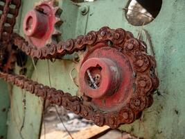 a rusty chain still attached to the red gear on an old machine with a faded green color photo