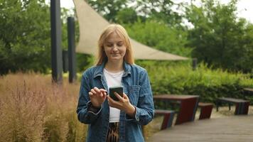 Happy pretty girl student hands user holding cell phone using education tech apps looking at smartphone texting messages standing outside. Mobile online applications concept. video