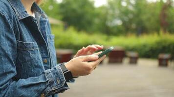 Happy pretty girl student hands user holding cell phone using education tech apps looking at smartphone texting messages standing outside. Mobile online applications concept. video