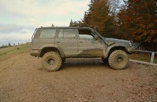 Automobile in a countryside landscape with a mud road. Off-road 4x4 suv automobile with ditry body after drive in muddy road photo
