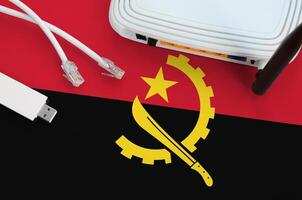 Angola flag depicted on table with internet rj45 cable, wireless usb wifi adapter and router. Internet connection concept photo