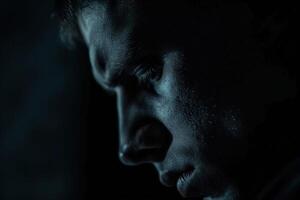 Close-up portrait of a man in a dark room, capturing deep emotions with visible stress lines and a contemplative gaze, highlighting themes of loneliness and introspection. Depression. photo