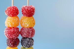 A cluster of colorful frozen berries on a stick rests on a blue background photo