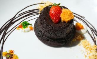 Delicious chocolate fondant or lava cake with cream, strawberry, and cake biscuit crumbles, Hot chocolate dessert pudding with liquid chocolate center, fondant au chocolate photo