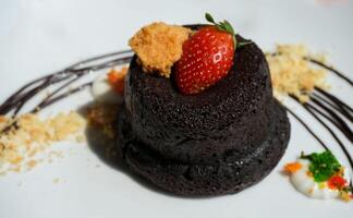Delicious chocolate fondant or lava cake with cream, strawberry, and cake biscuit crumbles, Hot chocolate dessert pudding with liquid chocolate center, fondant au chocolate photo