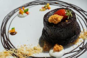 Delicious chocolate fondant or lava cake with cream, strawberry, and cake biscuit crumbles, Hot chocolate dessert pudding with liquid chocolate center, fondant au chocolate photo