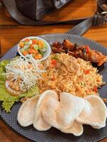 Fired rice or nasi goreng Indonesian chicken fried rice served with pickled cucumber and onion and chili with prawn crackers with satay as condiment photo