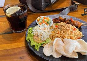 Fired rice or nasi goreng Indonesian chicken fried rice served with pickled cucumber and onion and chili with prawn crackers with satay as condiment photo