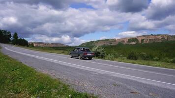 Cars drive along the road in the forest in the mountains. SCENE. The road passes between the trees in the forest. Blue mountains in the background. Warm weather in the forest and mountains video