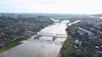 Russia.The view from the drone.Clip. A big city from a height where you can see summer houses and green trees around and a big bridge over the river that spreads and you can see the white fog over the video