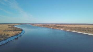 Aerial view of a wide rippled river with the endless pine tree forest and fields. Clip. Flying above summer nature with bushes and long river on blue cloudy sky background. video