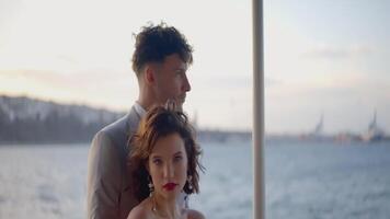 The bride and groom are hugging against the background of the waves. ACTION. The girl smiles and hugs the groom. A beautiful couple stands against the background of the sky and waves video