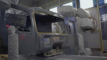 Robots at the factory paint the cab of the car. SCENE. At the factory, a white car is painted by robotic hands. On the assembly line, the car is painted in a light color. The car body is painted on video
