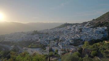 Bird's-eye view.Action. A beautiful landscape and a view of the city with small houses which is located on the mountains with green trees against the blue sky. video