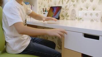 Making homework at a desk. Creative. A boy opens a drawer and taking a colorful notebook. video