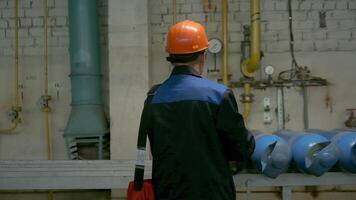 Worker at factory twists cylinders. Clip. Worker in helmet spins gas cylinders. Factory worker in helmet and uniform repairs and checks equipment video