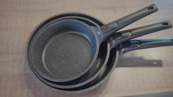 concepto de cocina utensilios, cerca arriba de nuevo conjunto de fritura sartenes acostado en el mesa. acción. nuevo moderno no palo sartenes video