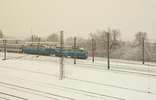 A long train of passenger cars is moving along the railway track. Railway landscape in winter after snowfall photo