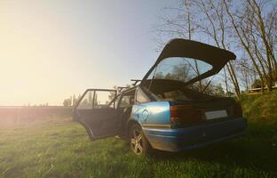 A blue car on a background of a rustic landscape with a wild cane field and a small lake. The family came to rest on the nature near the lake photo