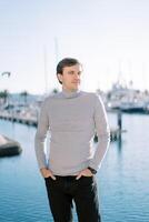 Young smiling man with his hands in his trouser pockets stands sideways on the embankment photo