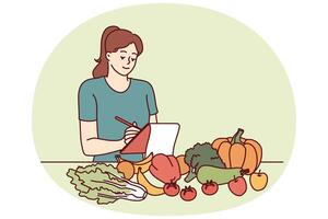 Woman nutritionist is standing near table with vegetables and making notes in notebook vector