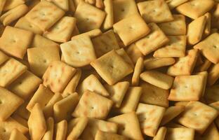 A lot of small cookies are square shaped. A pattern of a yellow salt cracker. Background image with salted pastry photo