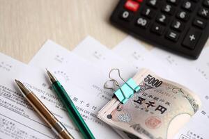 Japanese tax forms lies on table with calculator, pen and japanese yen money bills roll photo