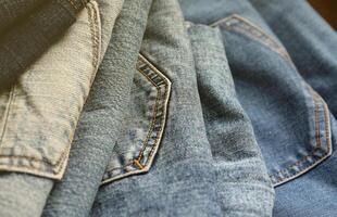 Many jeans in stack in wardrobe room. Row of pants denim jeans in closet. Concept of buy, sell, shopping and fashionable clothes photo