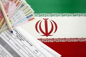 Iranian annual income tax return form F20-25-006 ready to fill on table with pen and iranian money on flag photo