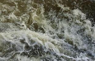 Waves of water of the river and the sea meet each other during high tide and low tide. Deep blue stormy sea water surface with white foam and waves pattern, background photo
